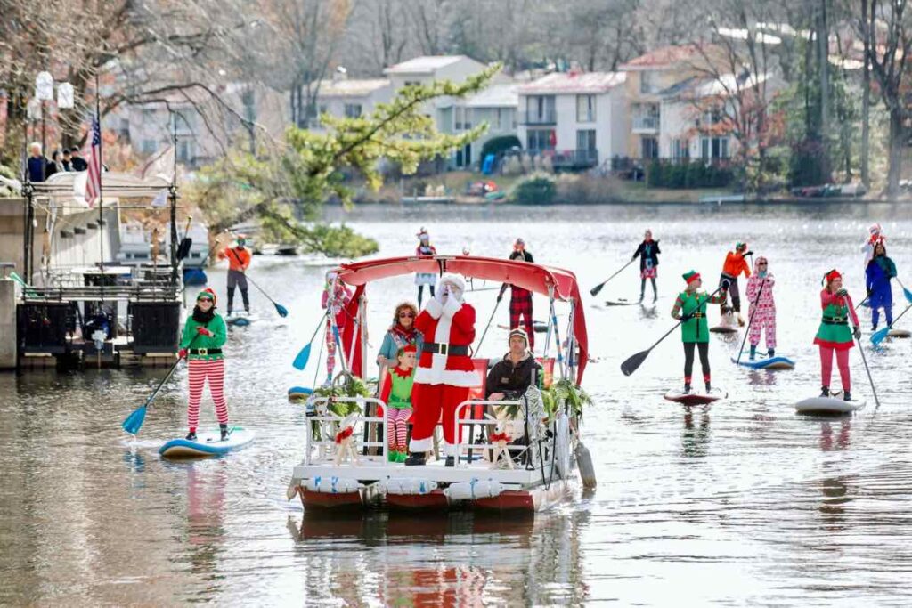 Santa arrives by boat with elves on SUPs atJingle on Lake Anne photo by Charlotte Geary Photography